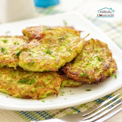 A plate of zucchini fritters made with the recipe on this page. Six fritters arranged on a white plate with a fork in the foreground.