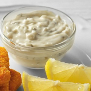 Small glass bowl of homemade tartar sauce with lemon and fried fish.