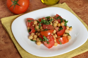 Tomato chickpea salad with strips of fresh basil on a white plate. 