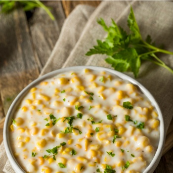Bowl of creamed corn with parsley garnish
