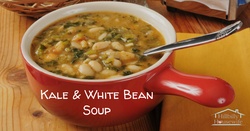 Kale and white bean soup in a red bowl on a wooden table.