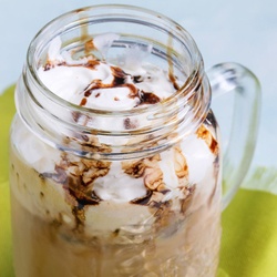 A mason jar of iced mocha topped with whipped cream and chocolate syrup.