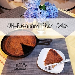 An old-fashioned pear cake baked in a cast iron skillet. A slice of the cake is cut and sits on a white plate with a fork. 