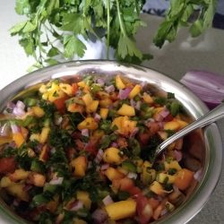 Fresh Peach Salsa Recipe- Tastes like Summer A bowl of fresh peach salad with a spoon. Herbs in the background