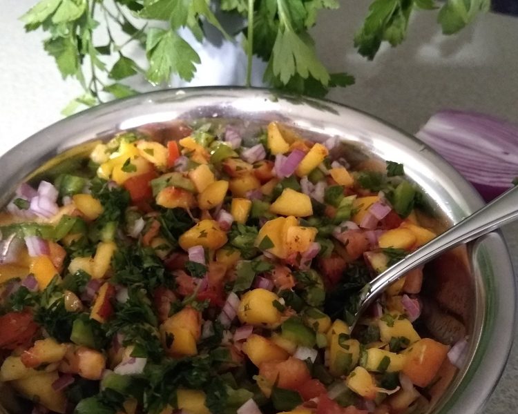 A bowl of fresh peach salad with a spoon. Herbs in the background