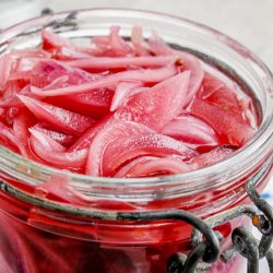 Closeup of a jar of pickled red onion slices.