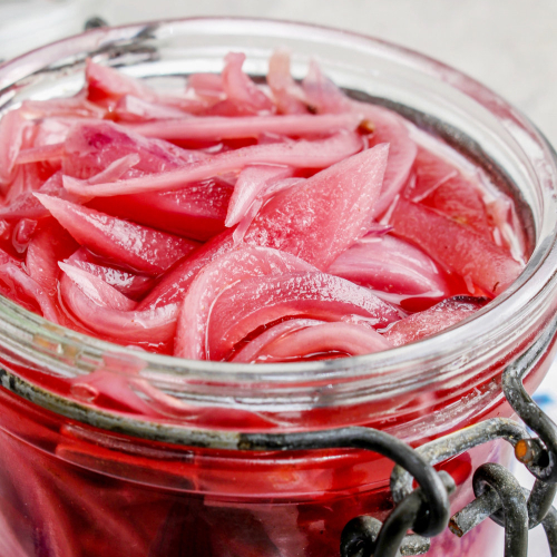 Closeup of a jar of pickled red onion slices.